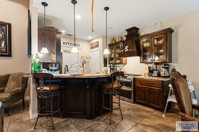 kitchen featuring a kitchen bar, premium range hood, range with two ovens, and hanging light fixtures