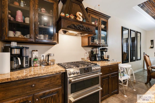 kitchen with custom range hood, light stone counters, stainless steel range, and dark brown cabinets