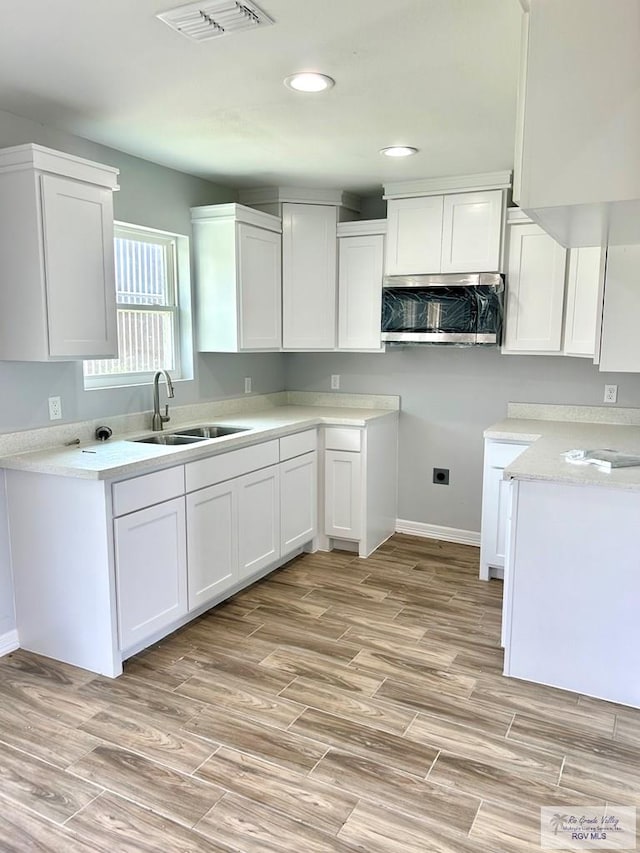 kitchen with white cabinets, light wood-type flooring, and sink