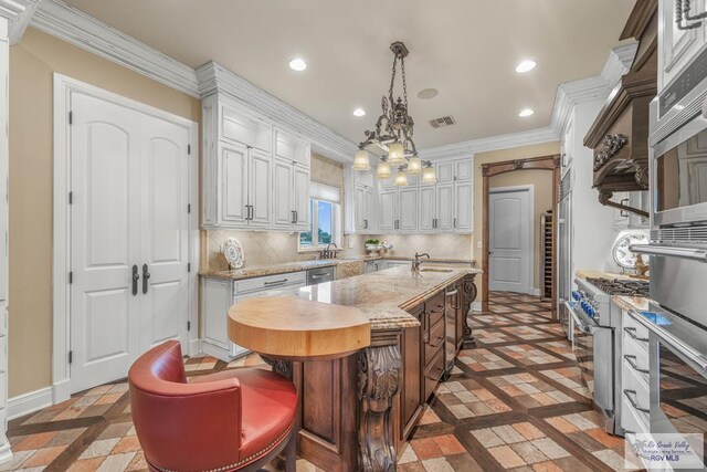 kitchen featuring tasteful backsplash, decorative light fixtures, a center island with sink, stainless steel appliances, and light stone countertops