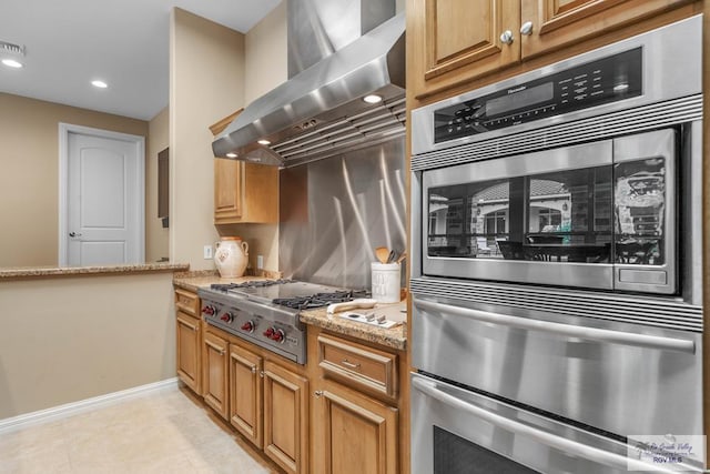 kitchen featuring appliances with stainless steel finishes, wall chimney exhaust hood, light stone countertops, and light tile patterned floors