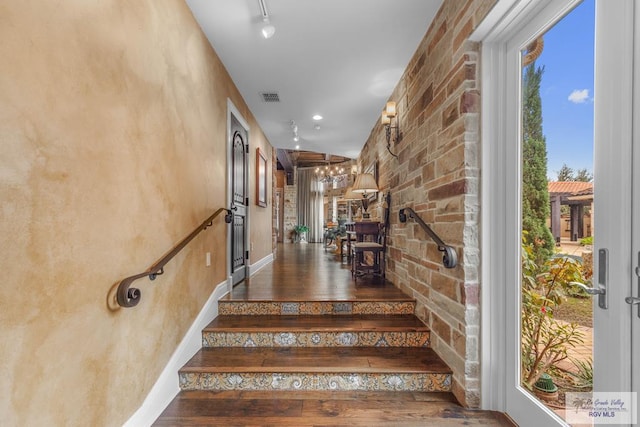 stairs featuring hardwood / wood-style flooring, rail lighting, and brick wall