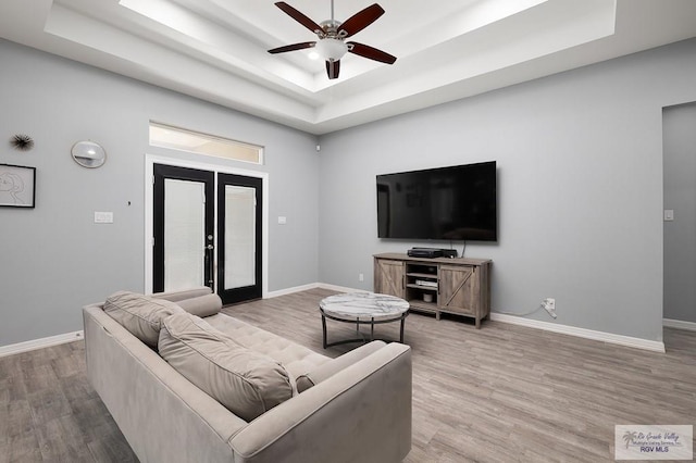 living area with light wood finished floors, a raised ceiling, and baseboards