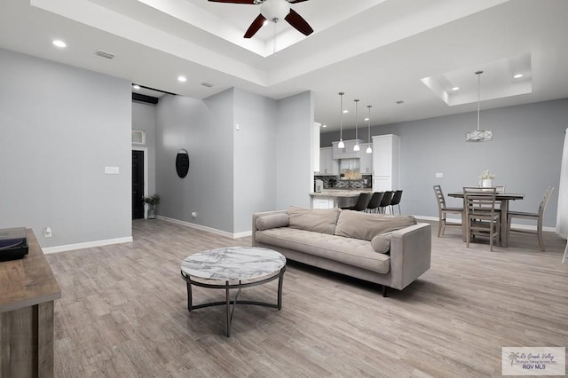 living area with a tray ceiling, light wood-style flooring, and baseboards