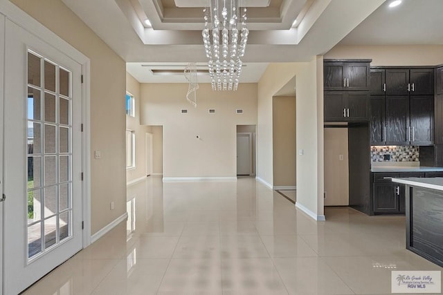 kitchen featuring light tile patterned floors, decorative backsplash, decorative light fixtures, a raised ceiling, and a chandelier