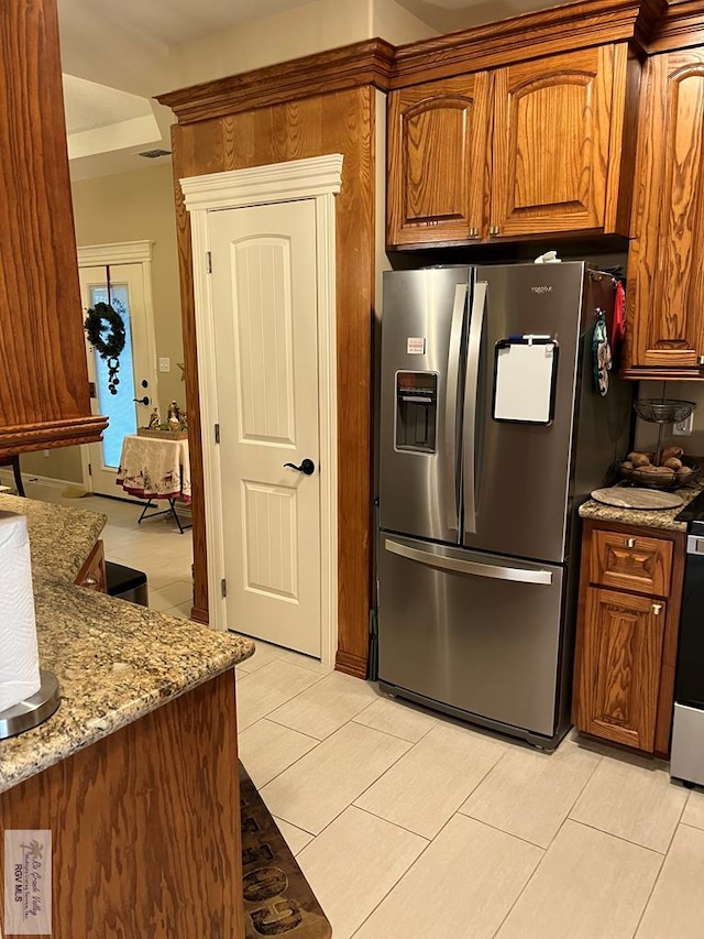 kitchen with stainless steel refrigerator with ice dispenser, light stone countertops, and light tile patterned floors