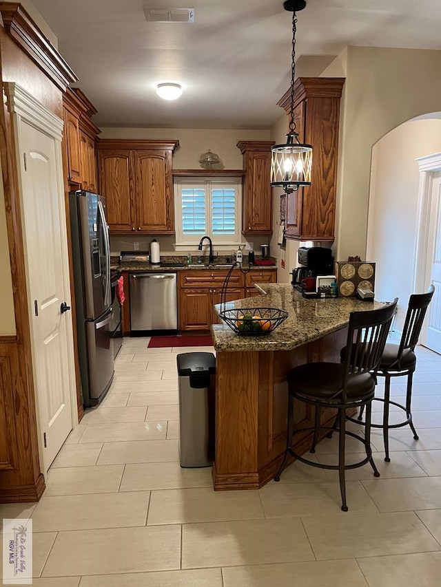 kitchen with sink, dark stone countertops, hanging light fixtures, stainless steel appliances, and a kitchen breakfast bar