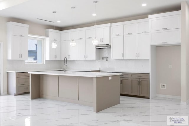 5359 Sidekick Ave, Brownsville, TX 78526 - kitchen with under cabinet range hood, recessed lighting, tasteful backsplash, light marble finish floors, and a center island with sink