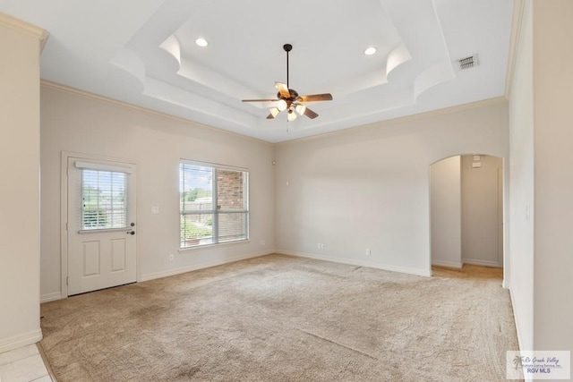 carpeted spare room with a tray ceiling, crown molding, and ceiling fan