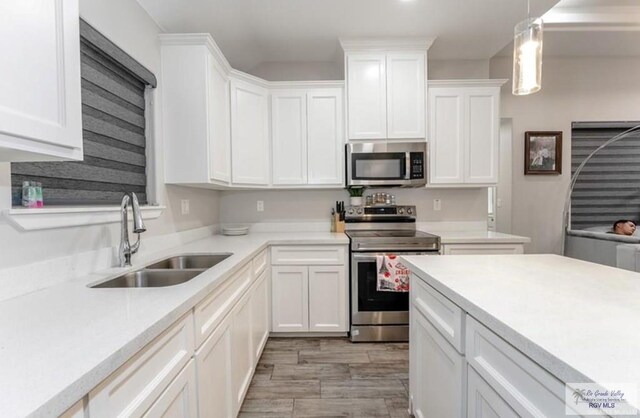 kitchen with appliances with stainless steel finishes, light wood-type flooring, sink, decorative light fixtures, and white cabinets