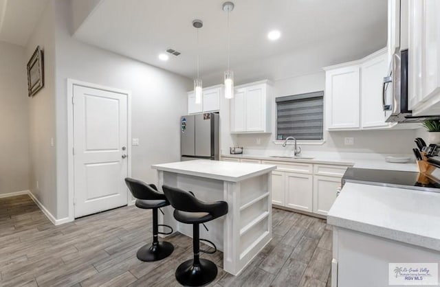 kitchen featuring sink, hanging light fixtures, a kitchen island, white cabinetry, and stainless steel appliances