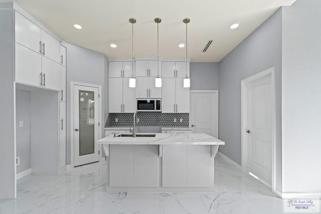 kitchen with sink, an island with sink, hanging light fixtures, and white cabinets