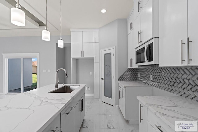 kitchen featuring white cabinetry, decorative light fixtures, sink, light stone counters, and decorative backsplash