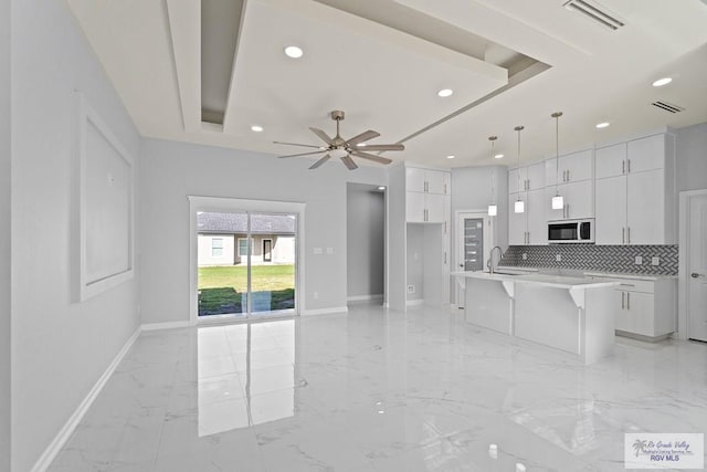 kitchen with pendant lighting, ceiling fan, white cabinets, a center island with sink, and decorative backsplash