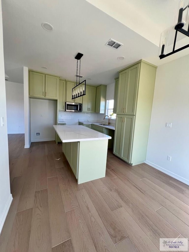 kitchen with stainless steel microwave, visible vents, a kitchen island, light wood-type flooring, and green cabinetry