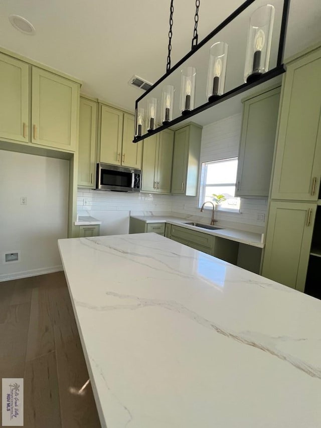 kitchen with stainless steel microwave, visible vents, decorative backsplash, a sink, and light stone countertops