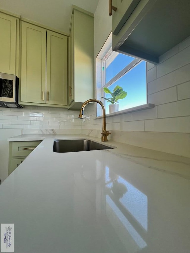 kitchen featuring tasteful backsplash, light countertops, stainless steel microwave, and a sink