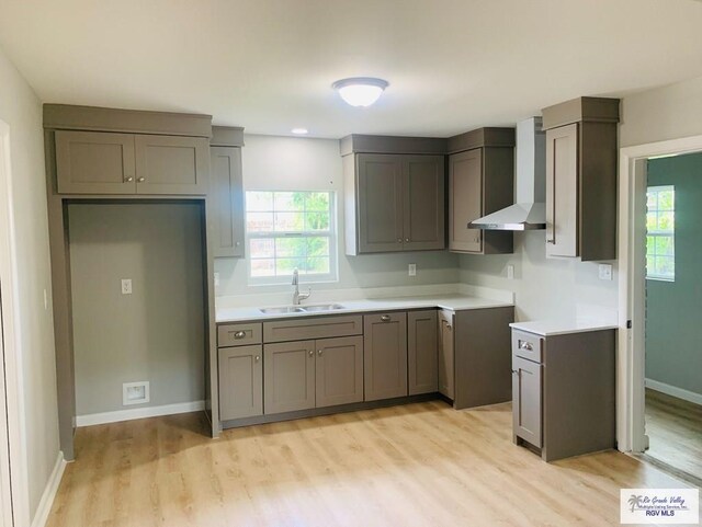 kitchen featuring wall chimney exhaust hood, gray cabinets, light wood-type flooring, and sink