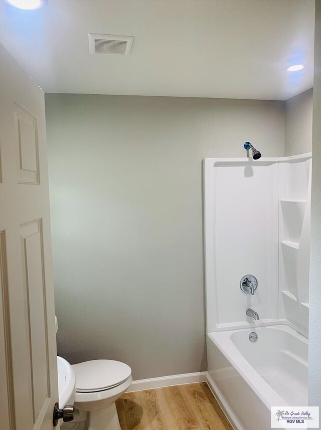 bathroom with hardwood / wood-style floors, toilet, and bathing tub / shower combination