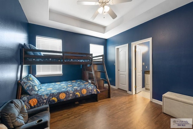 bedroom with a tray ceiling, multiple windows, ceiling fan, and hardwood / wood-style flooring