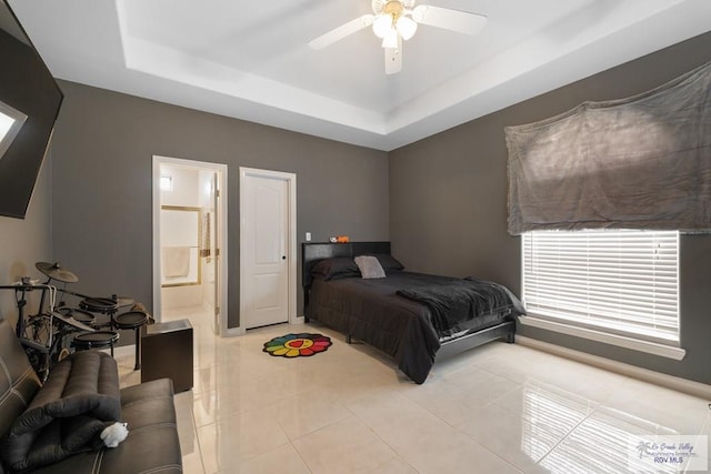 bedroom with light tile patterned floors, connected bathroom, a tray ceiling, and ceiling fan