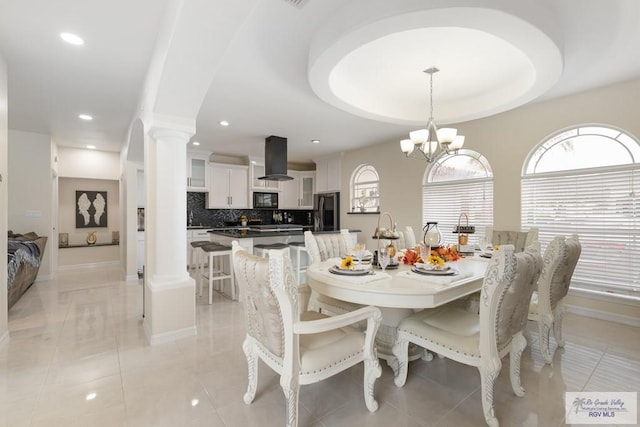 dining room with a chandelier, decorative columns, light tile patterned floors, and a tray ceiling