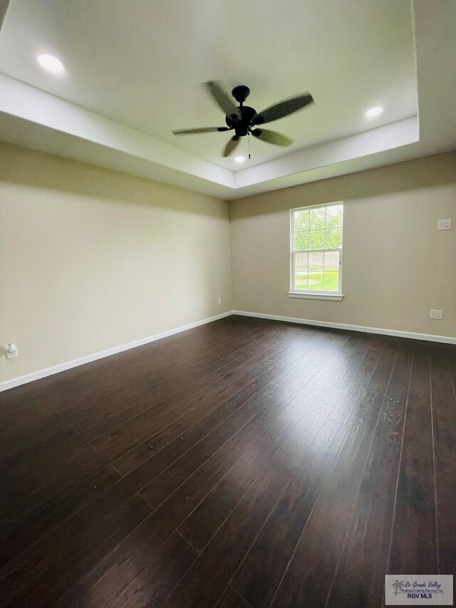 spare room with dark hardwood / wood-style floors, a raised ceiling, and ceiling fan