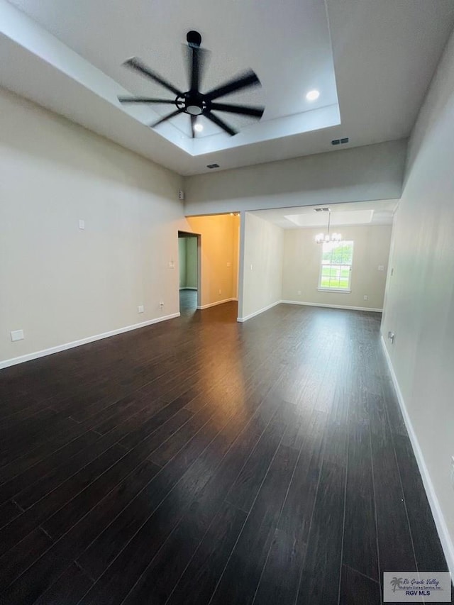spare room with a tray ceiling, dark wood-type flooring, and ceiling fan with notable chandelier