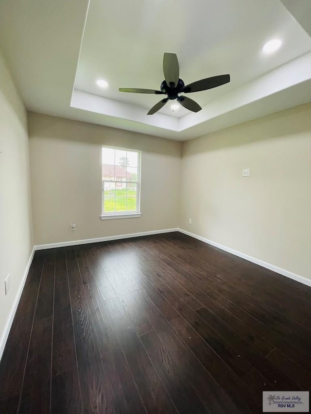spare room with ceiling fan, dark hardwood / wood-style flooring, and a tray ceiling