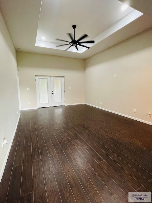 empty room featuring a raised ceiling, ceiling fan, and dark hardwood / wood-style flooring