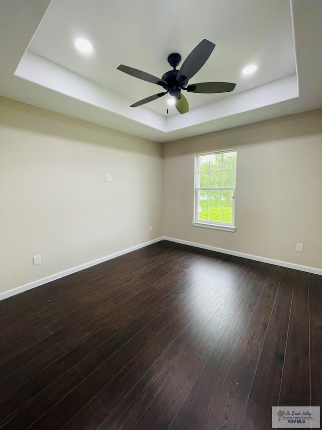 unfurnished room featuring a tray ceiling, ceiling fan, and dark hardwood / wood-style flooring