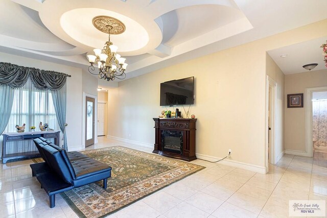 tiled living room featuring a tray ceiling, an inviting chandelier, and a wealth of natural light