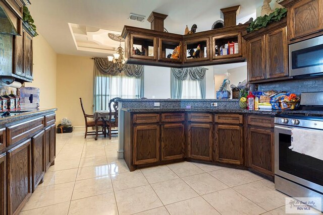 kitchen featuring decorative backsplash, dark stone countertops, light tile patterned floors, appliances with stainless steel finishes, and a notable chandelier