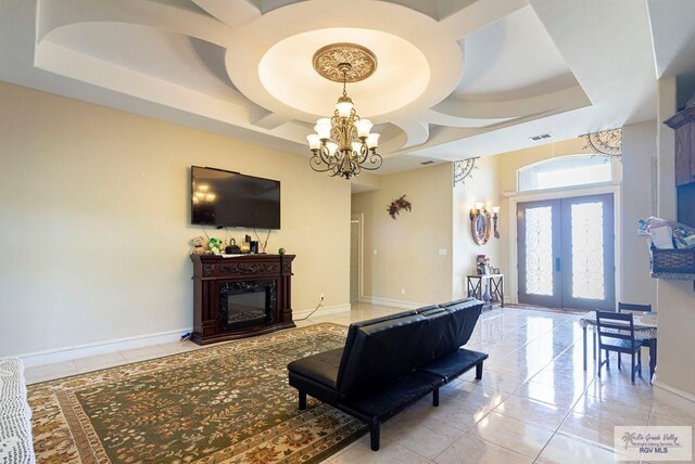 tiled living room with a tray ceiling, french doors, and an inviting chandelier