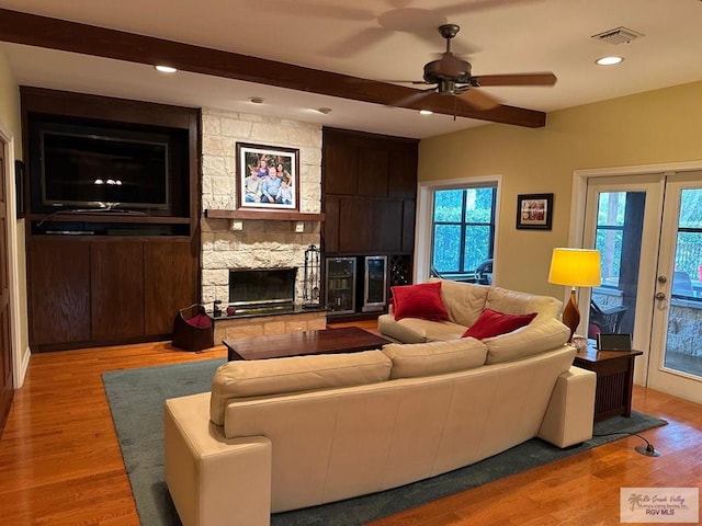 living room featuring a stone fireplace, beam ceiling, visible vents, and light wood-style floors