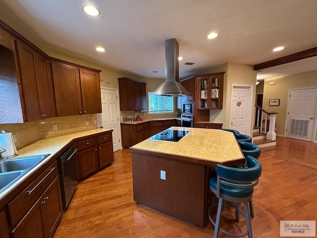 kitchen featuring island exhaust hood, light wood finished floors, stainless steel appliances, light countertops, and a kitchen island