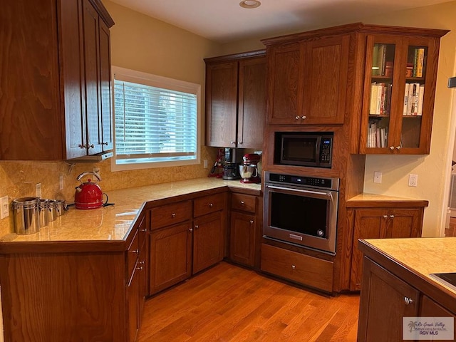 kitchen featuring black microwave, stainless steel oven, light countertops, light wood finished floors, and glass insert cabinets