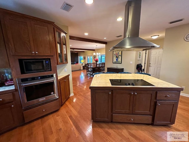 kitchen featuring a center island with sink, glass insert cabinets, island exhaust hood, light countertops, and black appliances