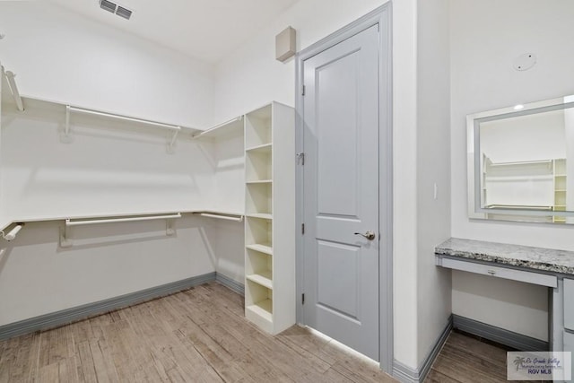 walk in closet with built in desk and light wood-type flooring