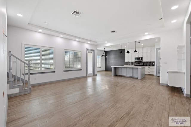 kitchen with tasteful backsplash, a center island, light hardwood / wood-style flooring, pendant lighting, and white cabinets