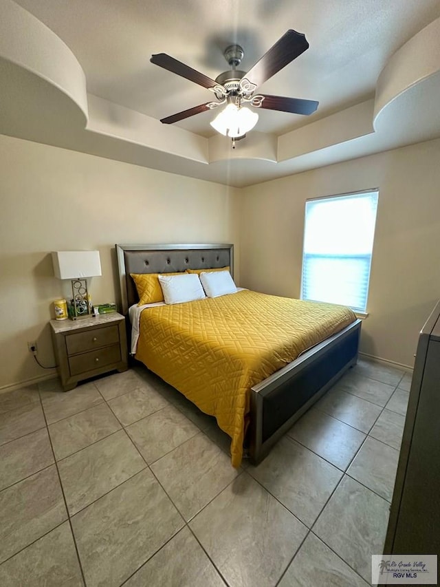 tiled bedroom with a tray ceiling and ceiling fan