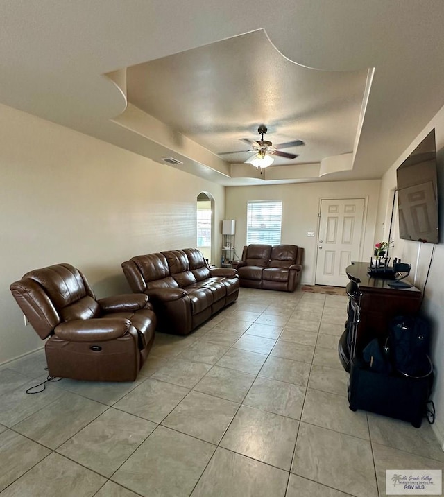 living room featuring light tile patterned floors, a tray ceiling, and ceiling fan