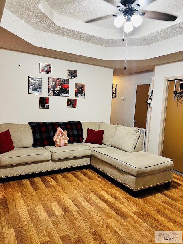 living room featuring hardwood / wood-style flooring, ceiling fan, a raised ceiling, and a textured ceiling