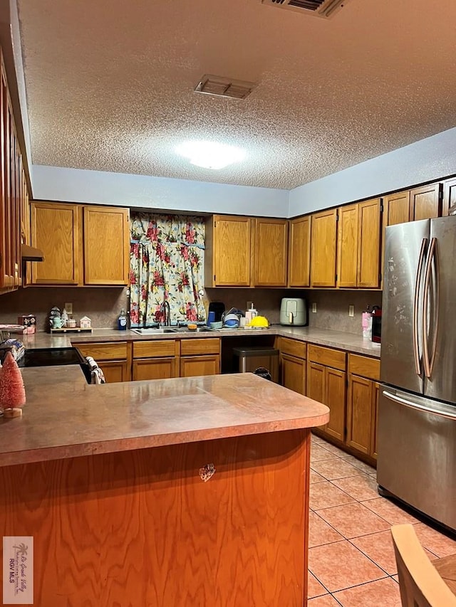 kitchen featuring stainless steel fridge, light tile patterned flooring, kitchen peninsula, and a textured ceiling