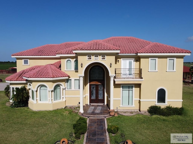 mediterranean / spanish-style home with a front yard, french doors, and a balcony