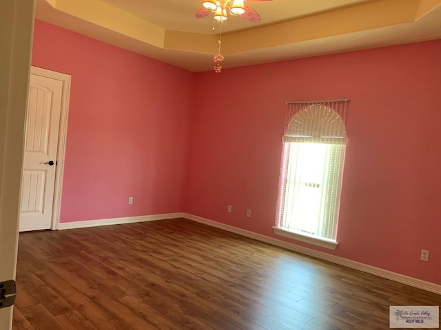 unfurnished room featuring a raised ceiling, ceiling fan, and dark wood-type flooring