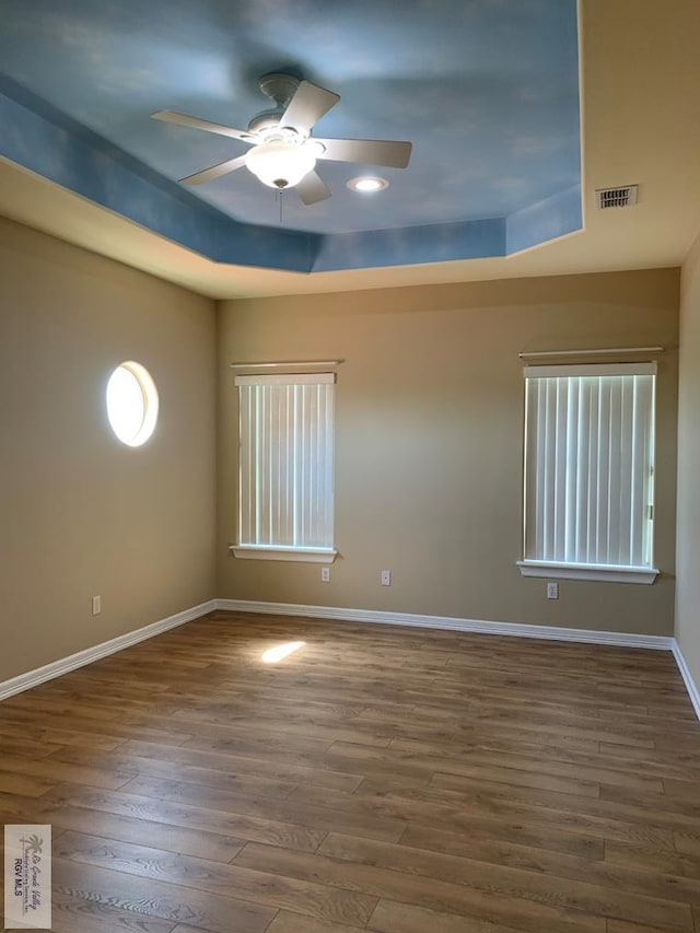 spare room featuring dark hardwood / wood-style floors, ceiling fan, and a tray ceiling