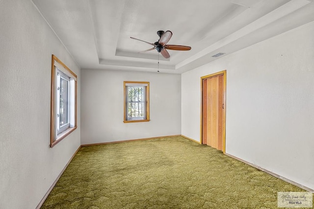 empty room with a raised ceiling, ceiling fan, and carpet floors