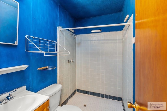 bathroom with a tile shower, vanity, a textured ceiling, and toilet