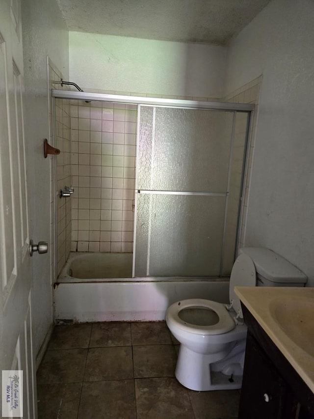 bathroom featuring combined bath / shower with glass door, tile patterned flooring, vanity, and toilet